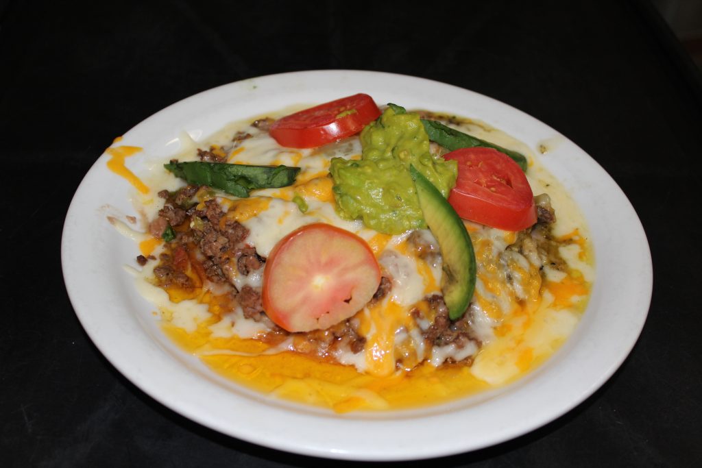 A delicious tostada covered in melted cheese topped with tomato and avocado.