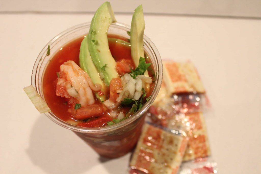 Shrimp Cocktail in a cup topped with avocado with saltine crackers on the side.