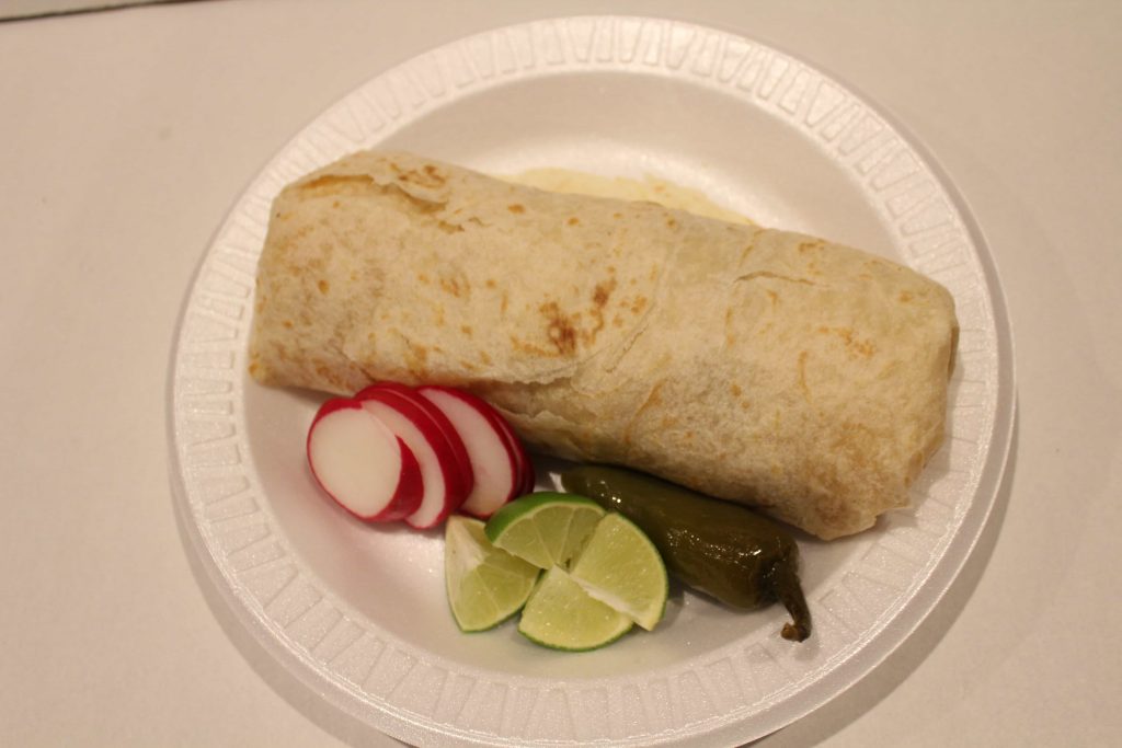 A burrito on a plate with lime, jalepeno, and sliced radishes.