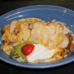 A burrito covered with melted cheese on a blue plate