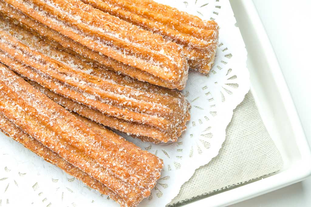 Churros covered in sugar sitting on a serving plate.